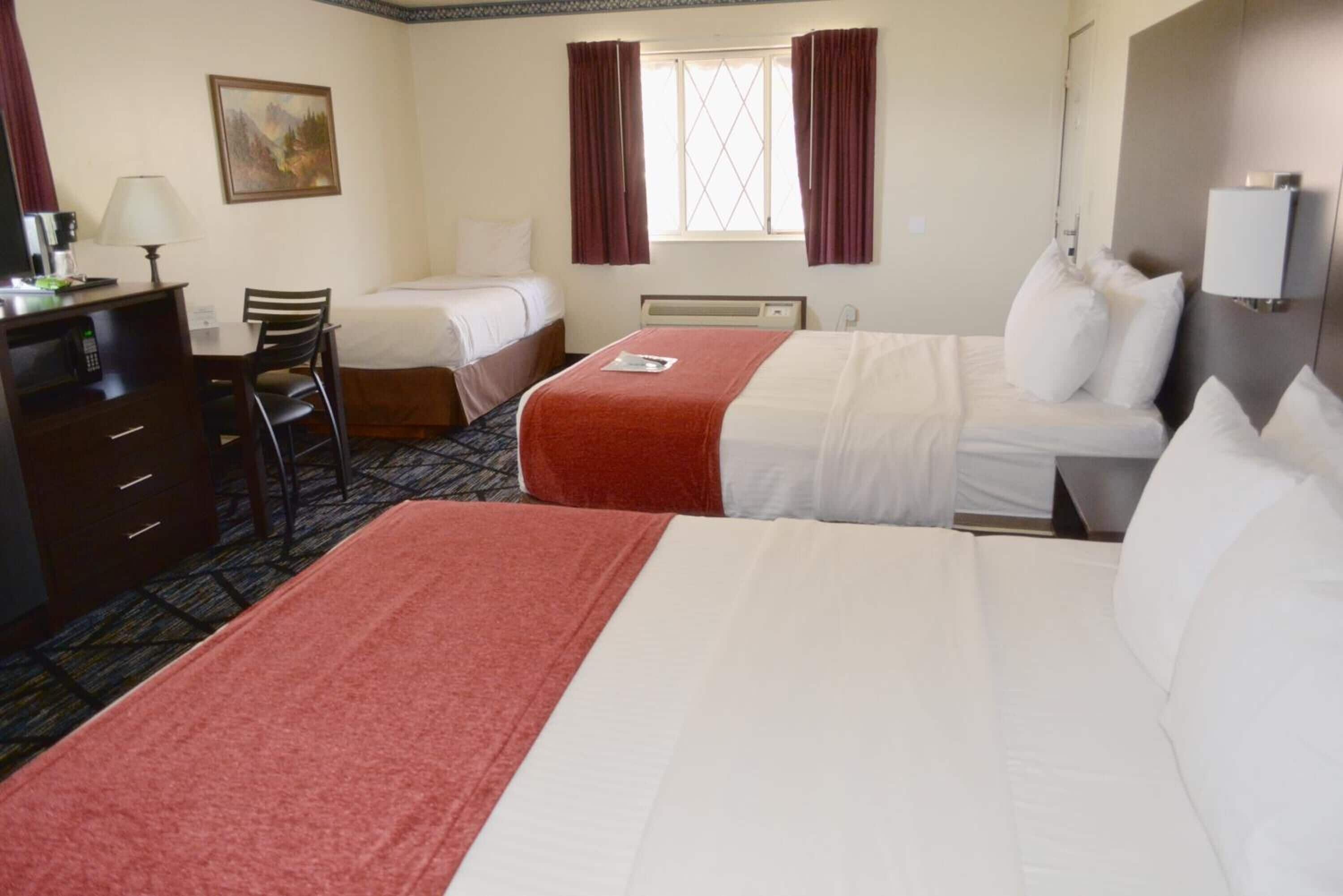 A hotel room with two beds, a desk with a chair, a dresser, and a window with curtains.