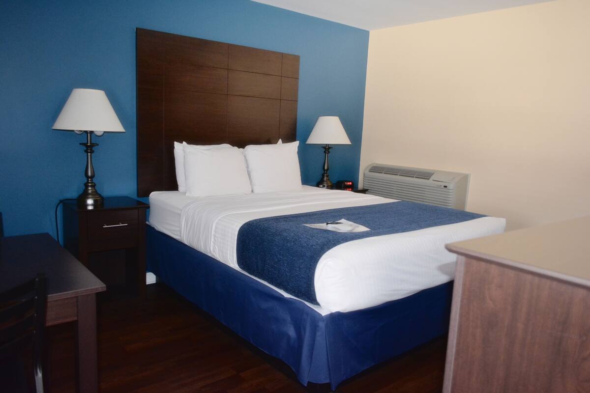 A hotel room with a bed, two bedside tables with lamps, a desk, and a chair.