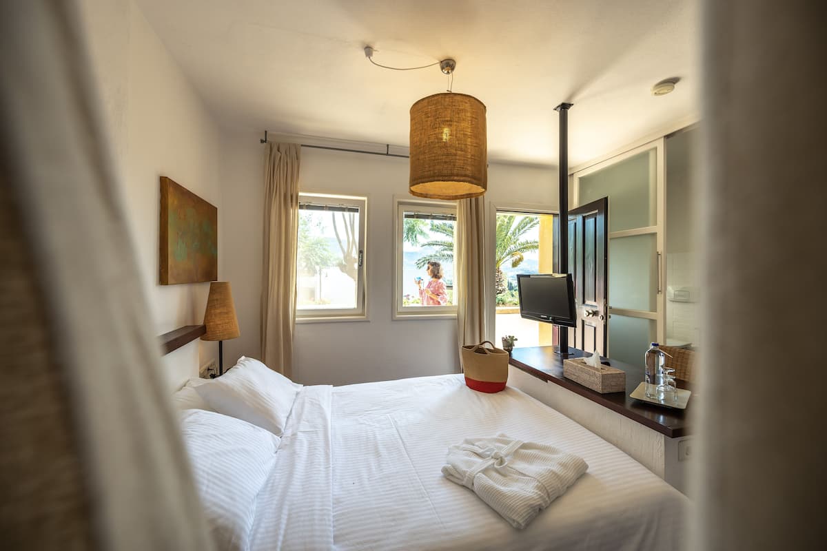 Quarto de hotel com cama, mesa de cabeceira, abajur, televisão e janela com cortinas.