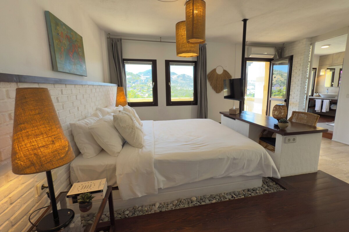 Un dormitorio moderno con una cama grande, un escritorio, una chimenea y vistas al exterior.