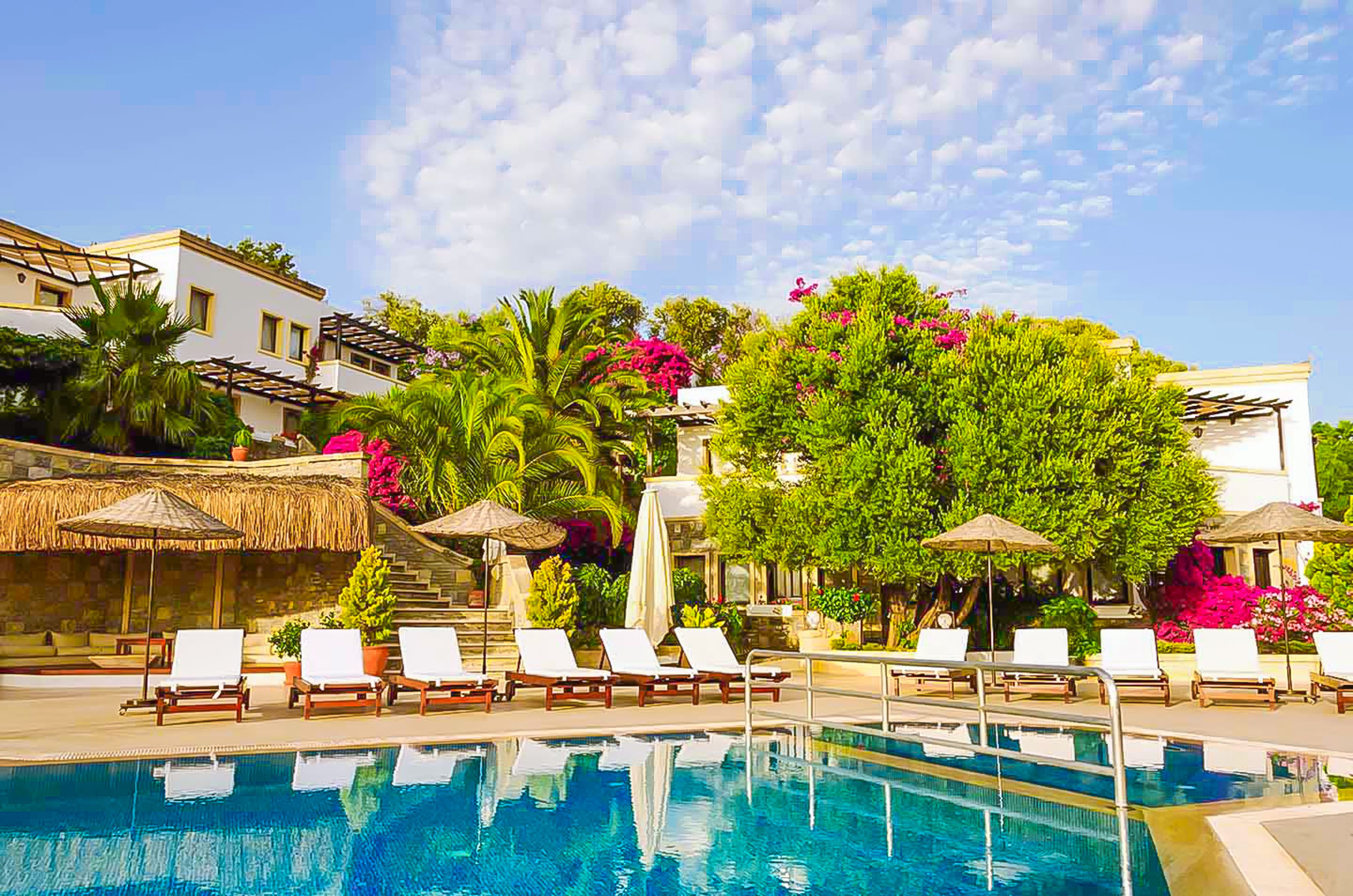 Uma área à beira da piscina com espreguiçadeiras, guarda-sóis e uma piscina azul cristalina.