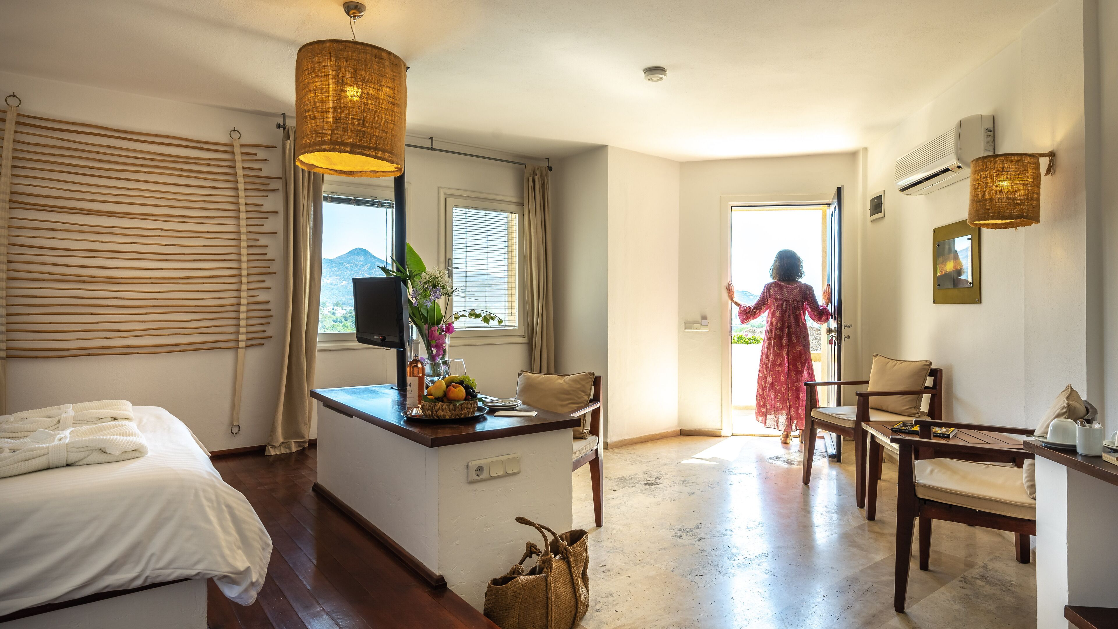 A hotel room with a bed, a desk with a computer, a chair, a dining table, and a view of the outdoors.
