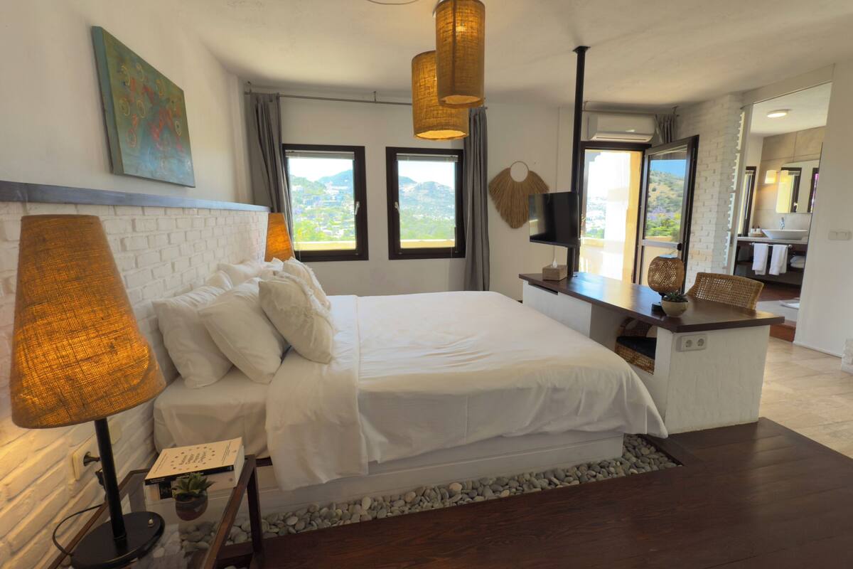 Quarto moderno com cama grande, escrivaninha, lareira e vista para o exterior.