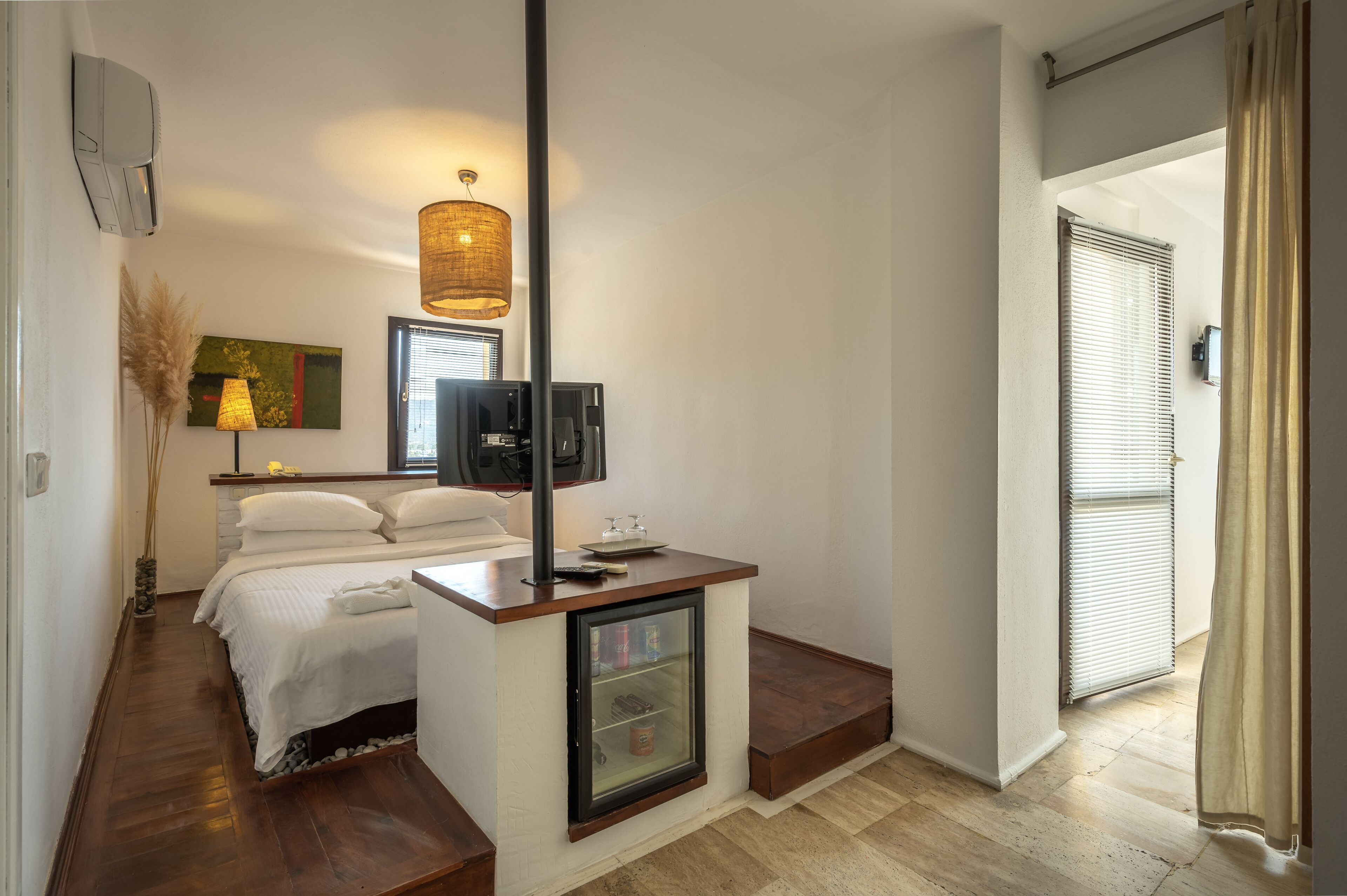 A compact hotel room with a bed, bedside table, TV, and a small refrigerator.