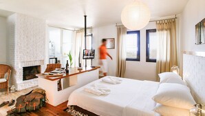 A hotel room with a fireplace, a bed with white linens, a wooden floor, and a large window with curtains. - 4Reasons Hotel And Bistro | 12+ (Bodrum)
