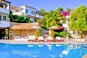 A swimming pool with lounge chairs and umbrellas, surrounded by lush greenery and a multi-story building. - 4Reasons Hotel And Bistro | 12+ (Bodrum)