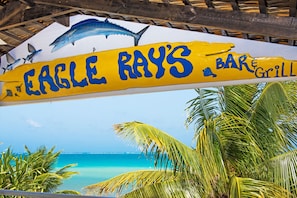 A beachside bar named Eagle Ray's Bar & Grill with a sign featuring a shark and palm trees. - Compass Point Dive Resort (East End)