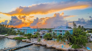 A coastal resort with multiple blue buildings, a sandy beach, and a dock extending into the water. - Compass Point Dive Resort (East End)