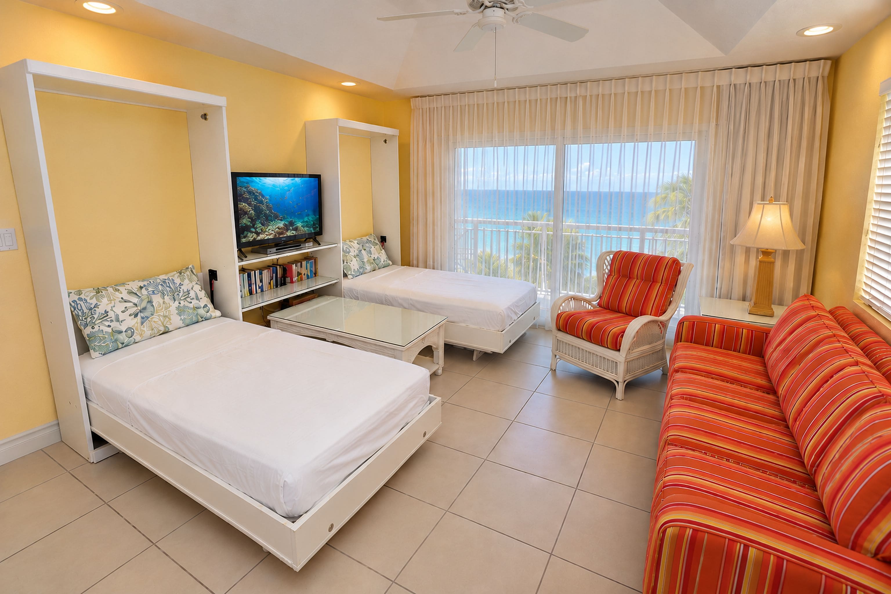 A hotel room with two beds, a sofa, a television, and a view of the ocean.
