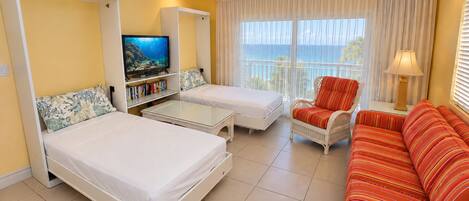 A hotel room with two beds, a sofa, a television, and a view of the ocean.