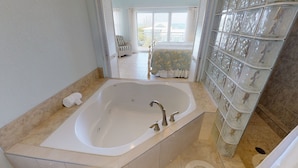 A bathroom with a large bathtub, a glass shower enclosure, and a view of a balcony with a chair. - Compass Point Dive Resort (East End)