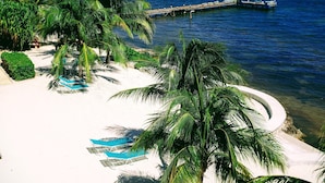A beach with white sand, palm trees, and a pier extending into the ocean. - Compass Point Dive Resort (East End)