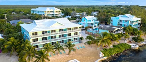 A beachfront hotel with multiple buildings, a sandy beach, and palm trees.