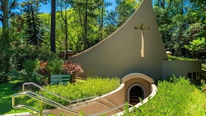 Una capilla con una cruz, rodeada de follaje y árboles.