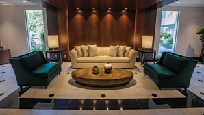 Una sala moderna con un sofá color beige, dos sillones verdes y una mesa de centro redonda con jarrones decorativos.