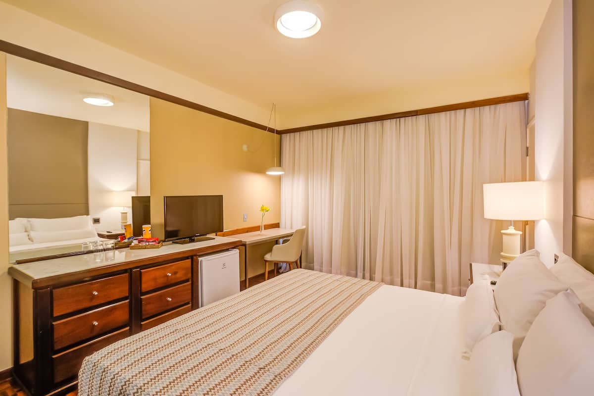 A hotel room with a bed, a desk, a chair, a dresser, a mirror, and a window with curtains.