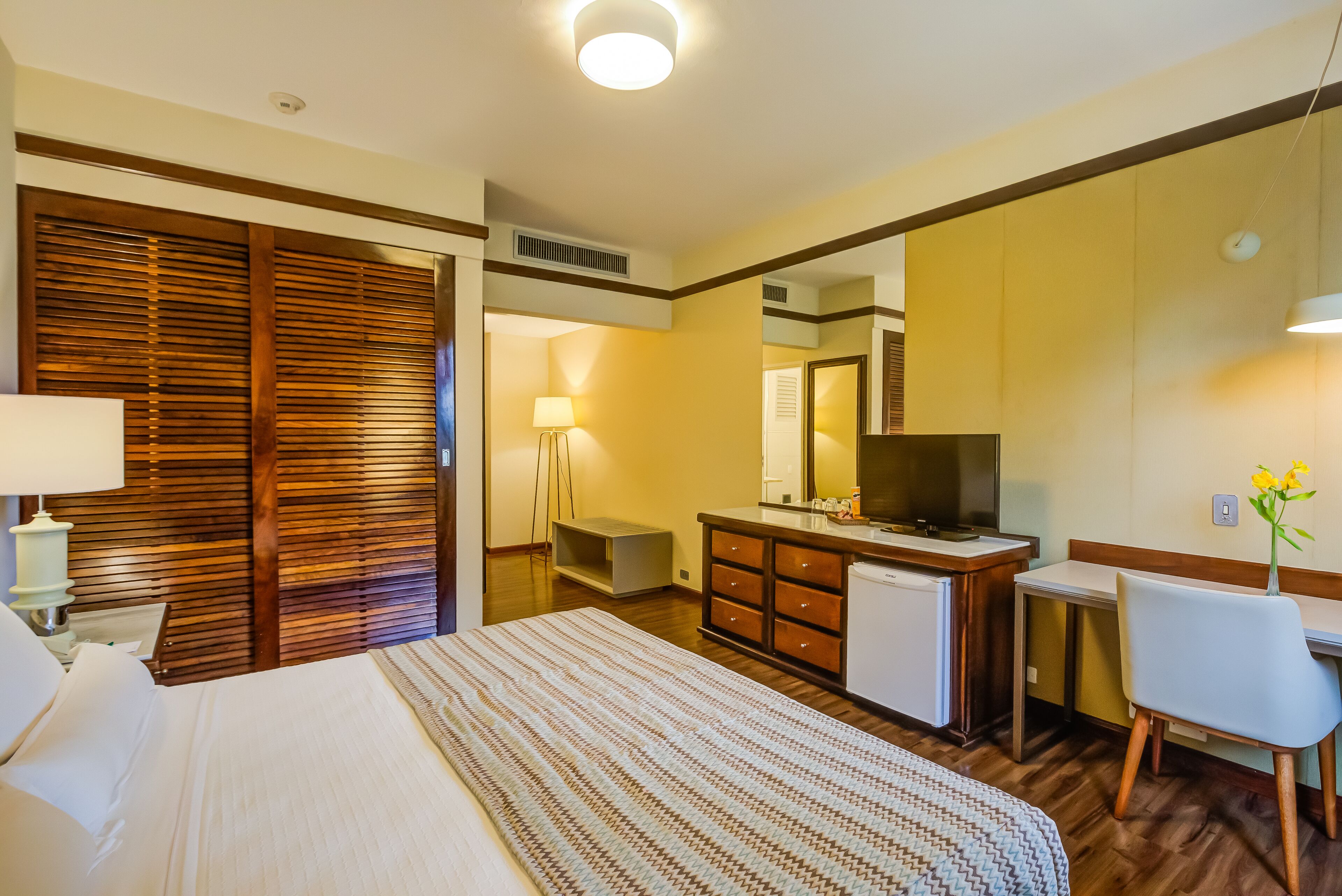 A hotel room with a bed, a desk, a chair, a dresser, a television, and a mirror.