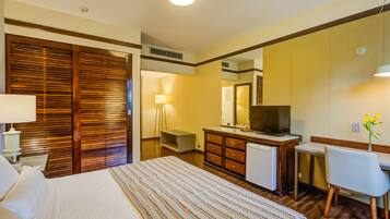 A hotel room with a bed, a desk, a chair, a dresser, a television, and a mirror.