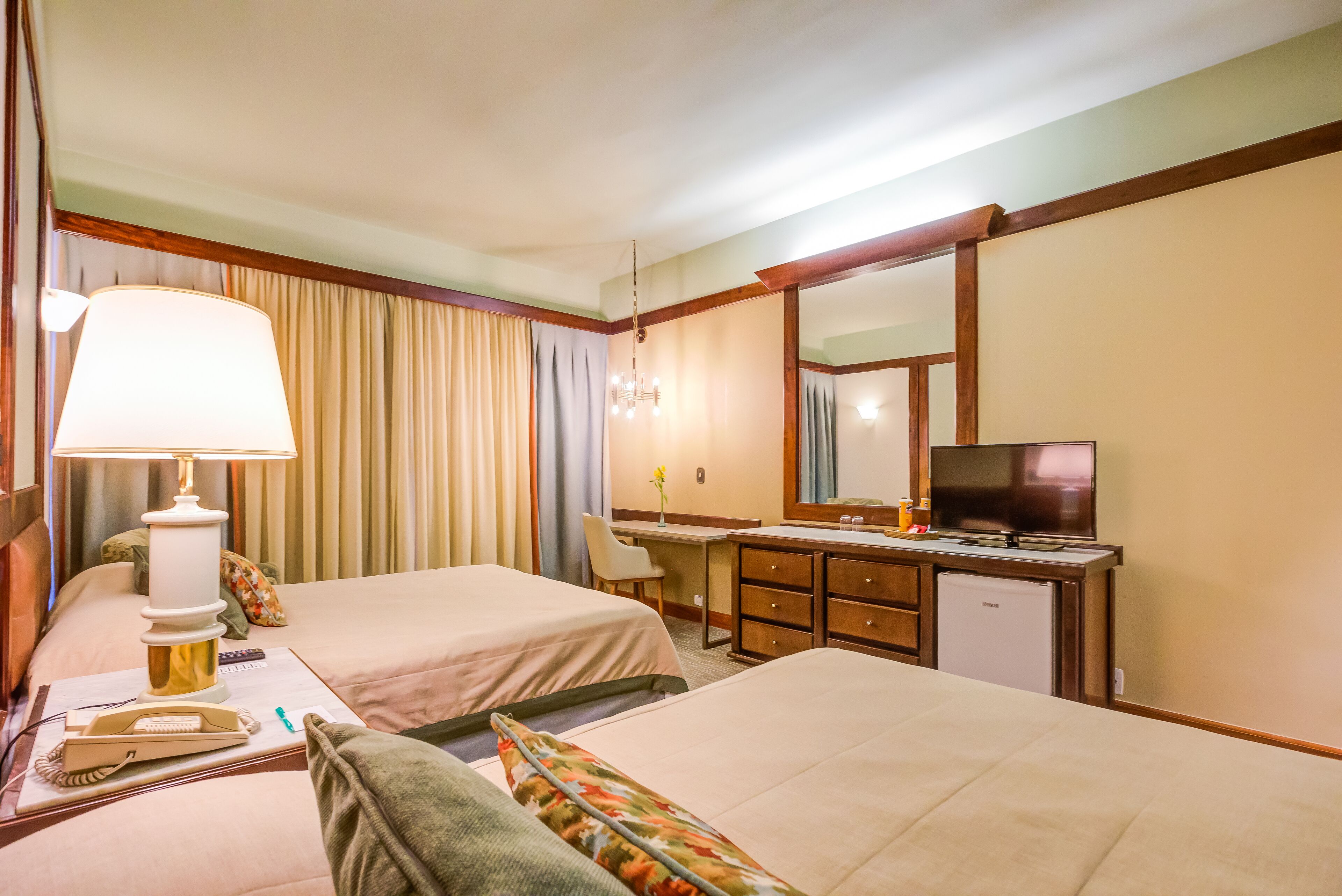 Ein Hotelzimmer mit zwei Betten, einem Schreibtisch, einem Fernseher, einer Lampe und einem kleinen Kühlschrank.