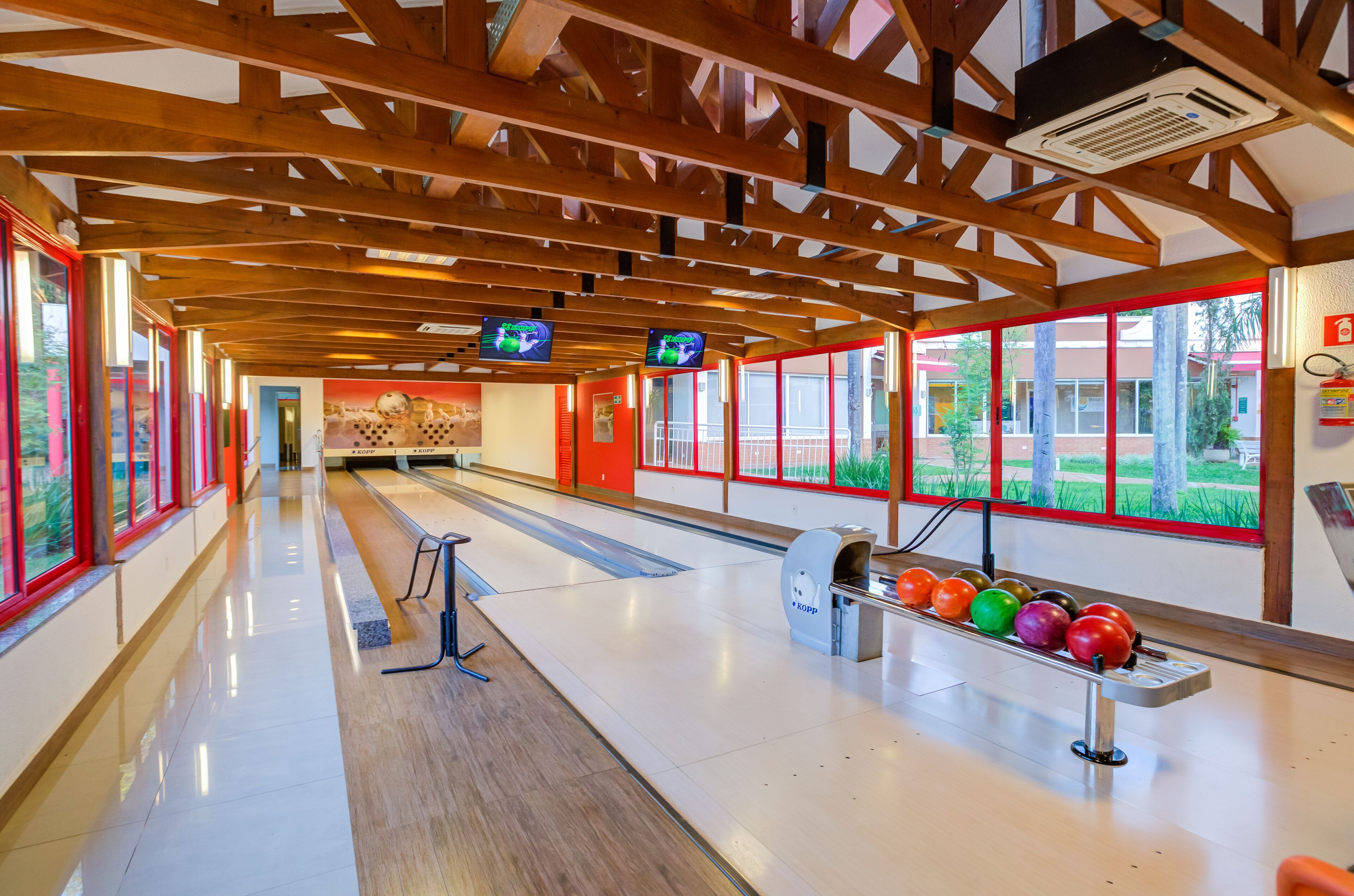 A bowling alley with wooden beams, a polished floor, and a row of colorful bowling balls.