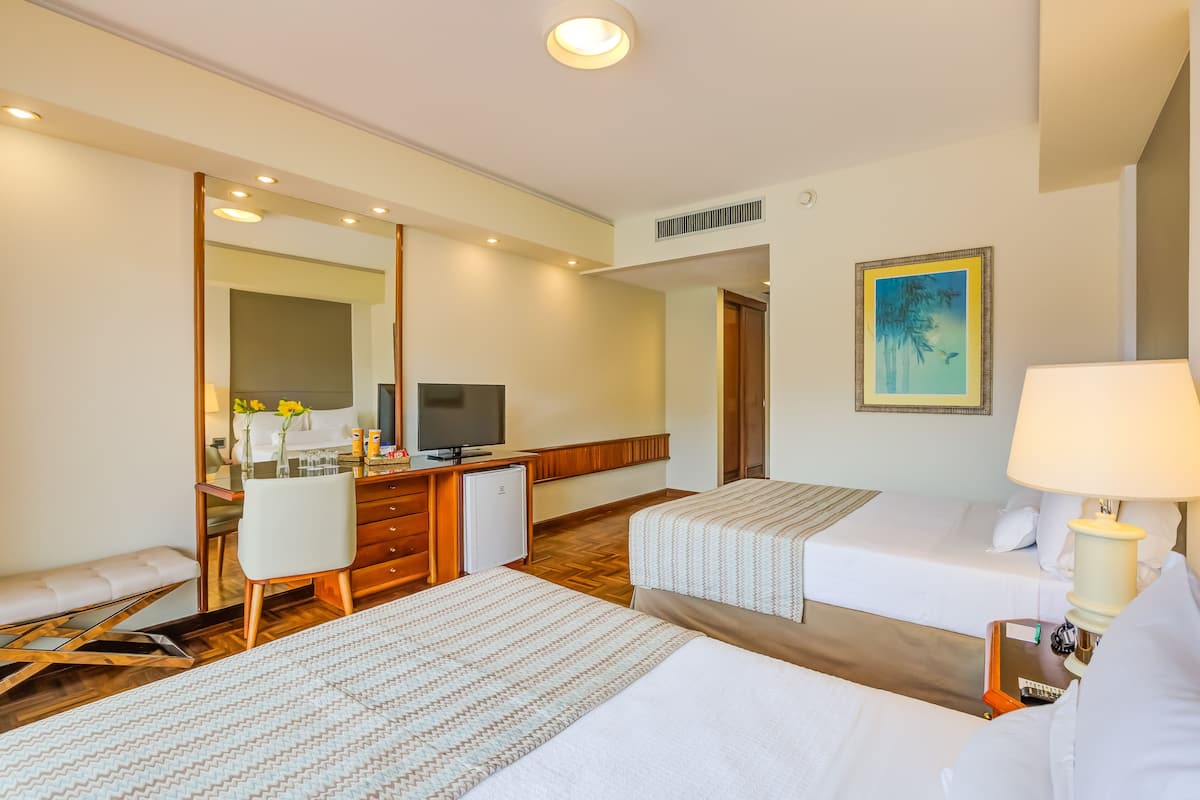 A hotel room with two beds, a desk with a TV, a mirror, and a painting on the wall.