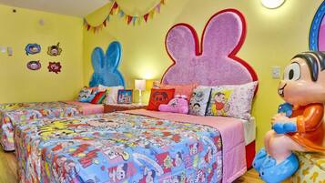 Une pièce aux couleurs vives, avec deux lits, chacun recouvert d’une couverture aux motifs colorés inspirés de bandes dessinées. Les murs sont décorés de personnages de dessins animés et une grande tête de lapin orne le haut du lit.