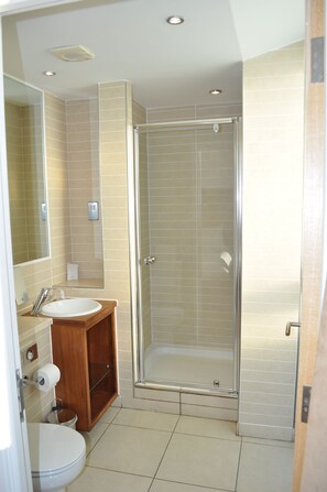 Une salle de bain comprenant des toilettes, un lavabo, un miroir et une douche fermée par des parois en verre.
