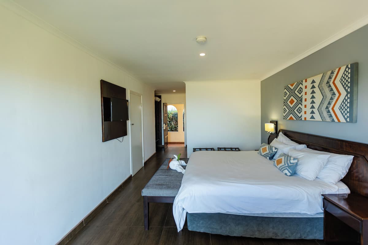 A hotel room with a large bed, a bedside table, a wall-mounted TV, and a patterned wall decoration.