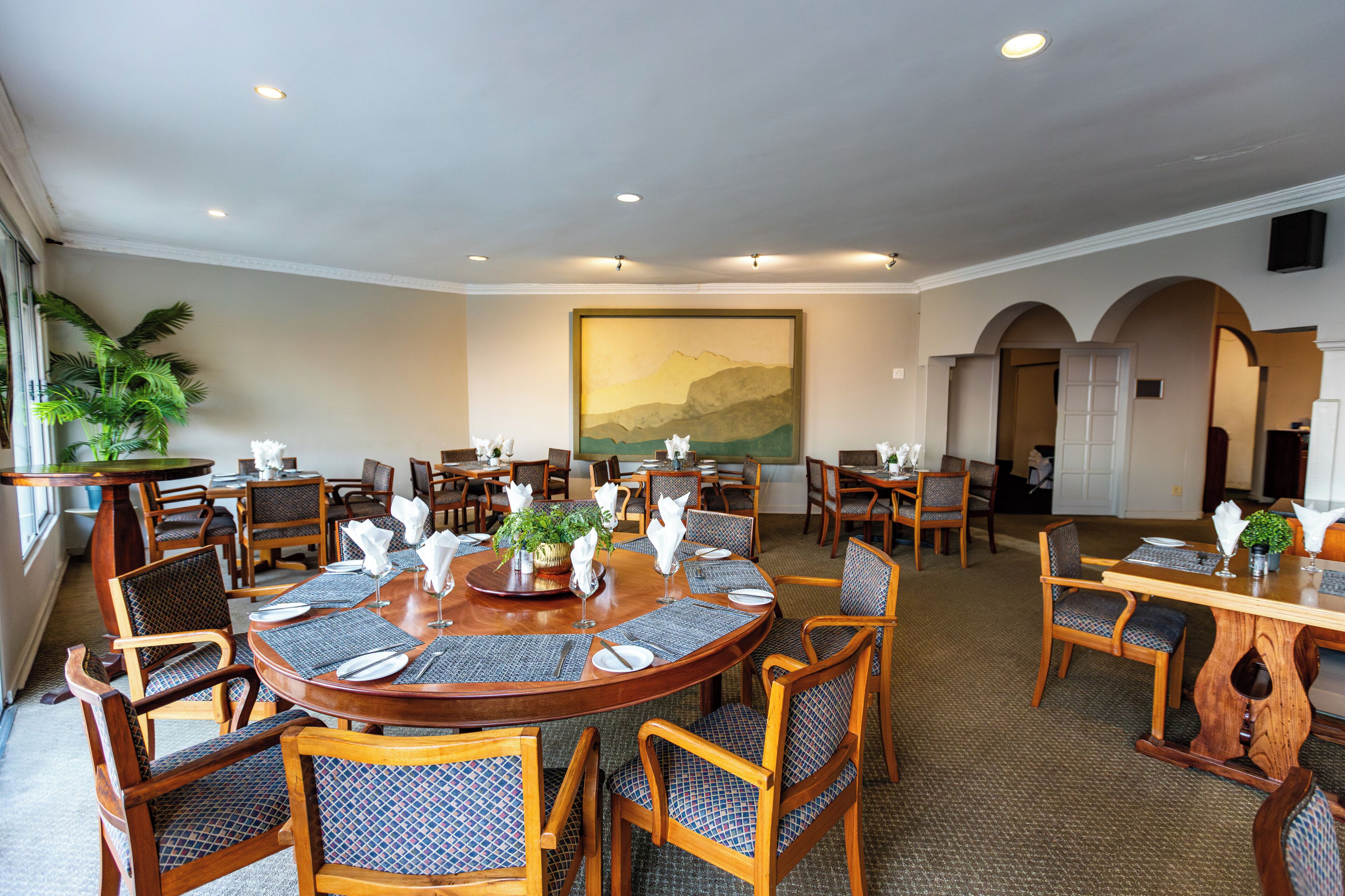 A conference room with round tables, chairs, and a large painting on the wall.