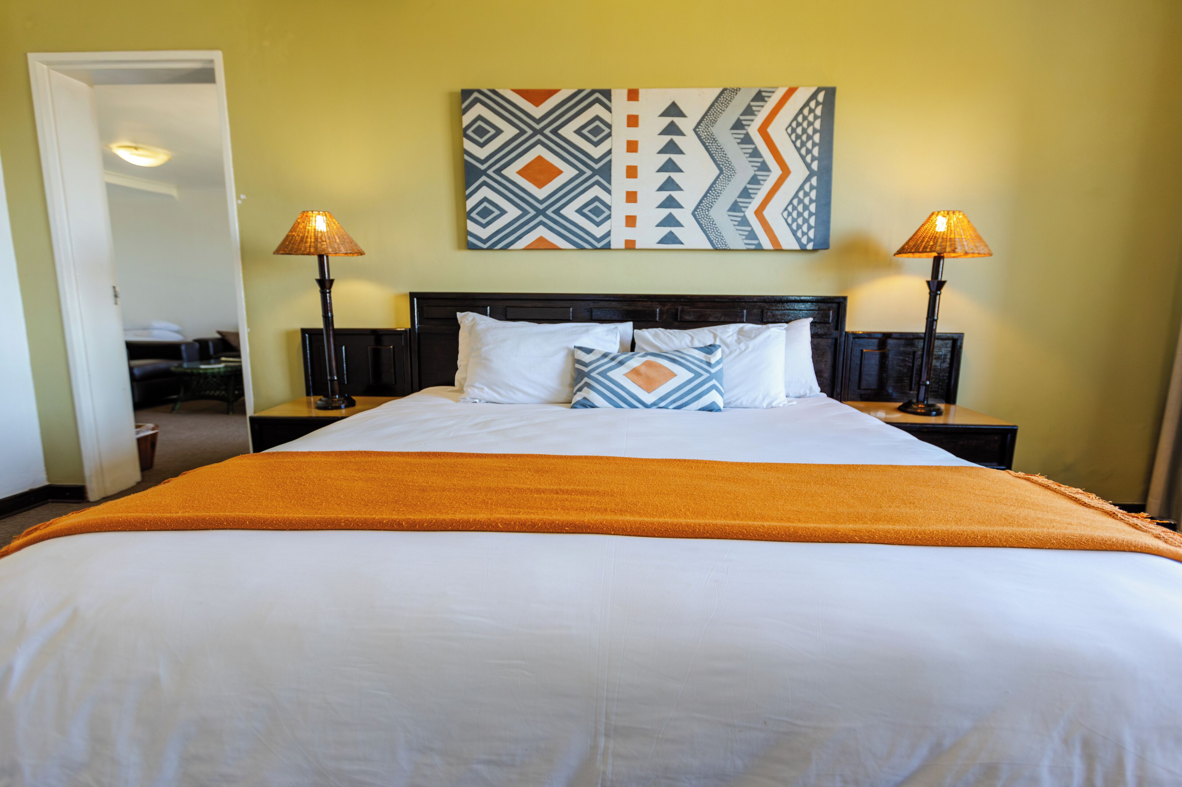 A hotel room with a large bed, two bedside lamps, a headboard, and a wall-mounted artwork.