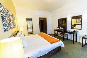 A hotel room with a bed, desk, chair, and a large mirror.
