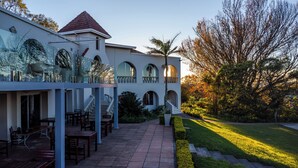 A multi-story building with a balcony, outdoor seating, and a well-maintained garden. -  Mountain View International Hotel (Mbabane)