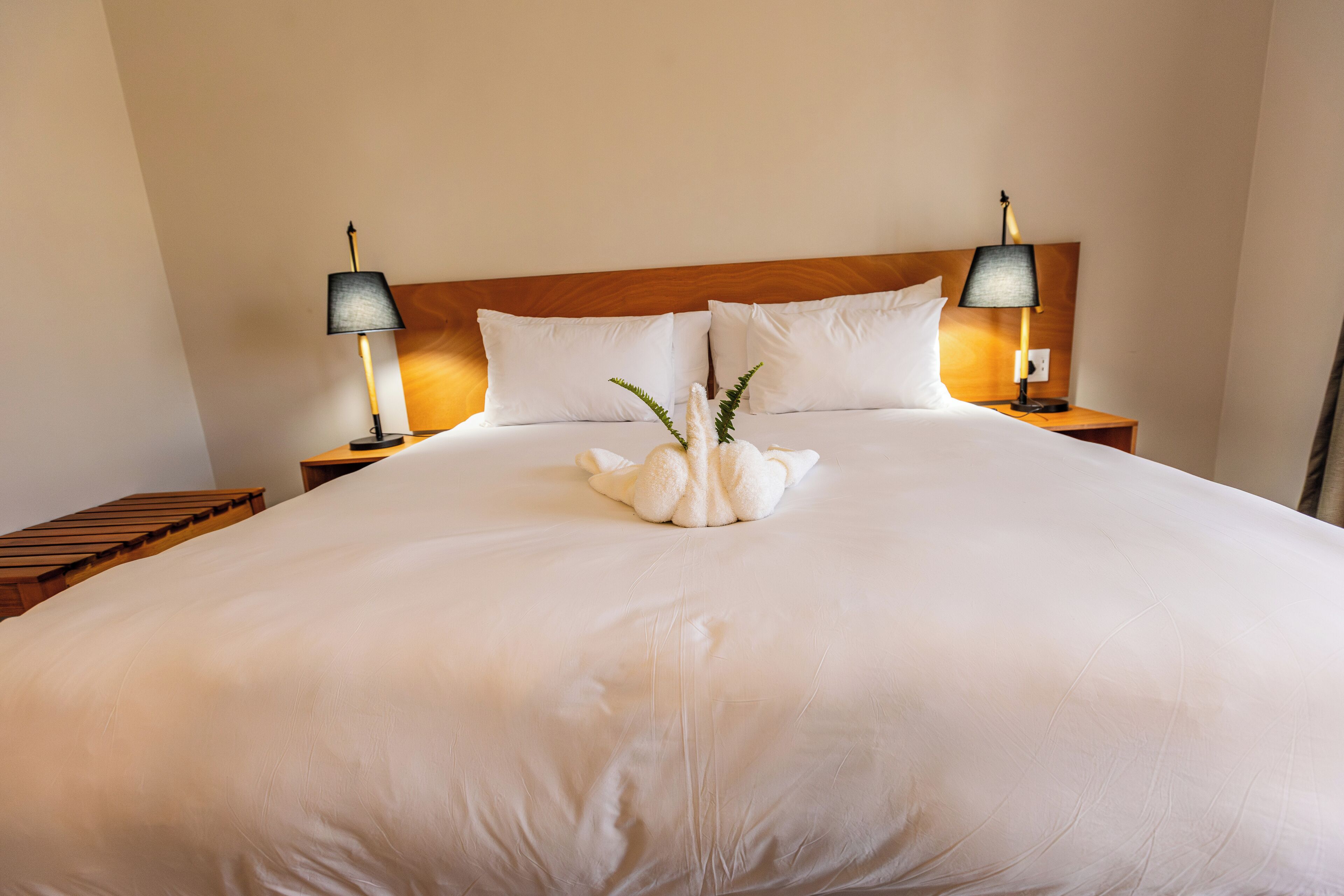 A large bed with white linens, two bedside lamps, and a wooden headboard.