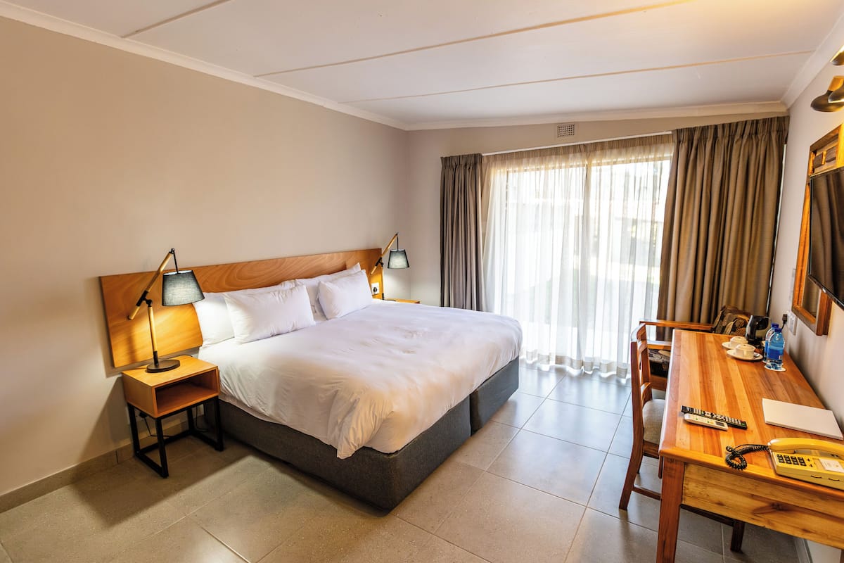 A hotel room with a bed, bedside tables, a desk, and a chair.