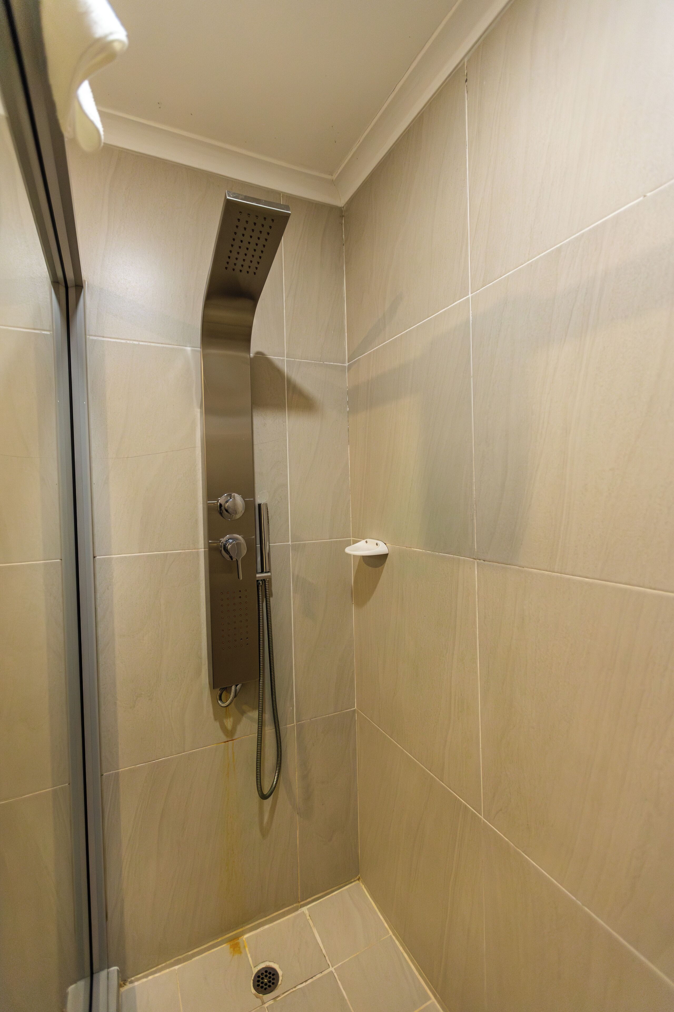 A shower with a handheld showerhead, a wall-mounted faucet, and a small shelf.