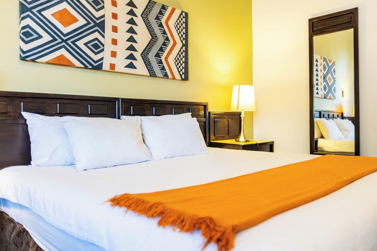 A hotel room with a large bed, a nightstand with a lamp, and a wall-mounted mirror.