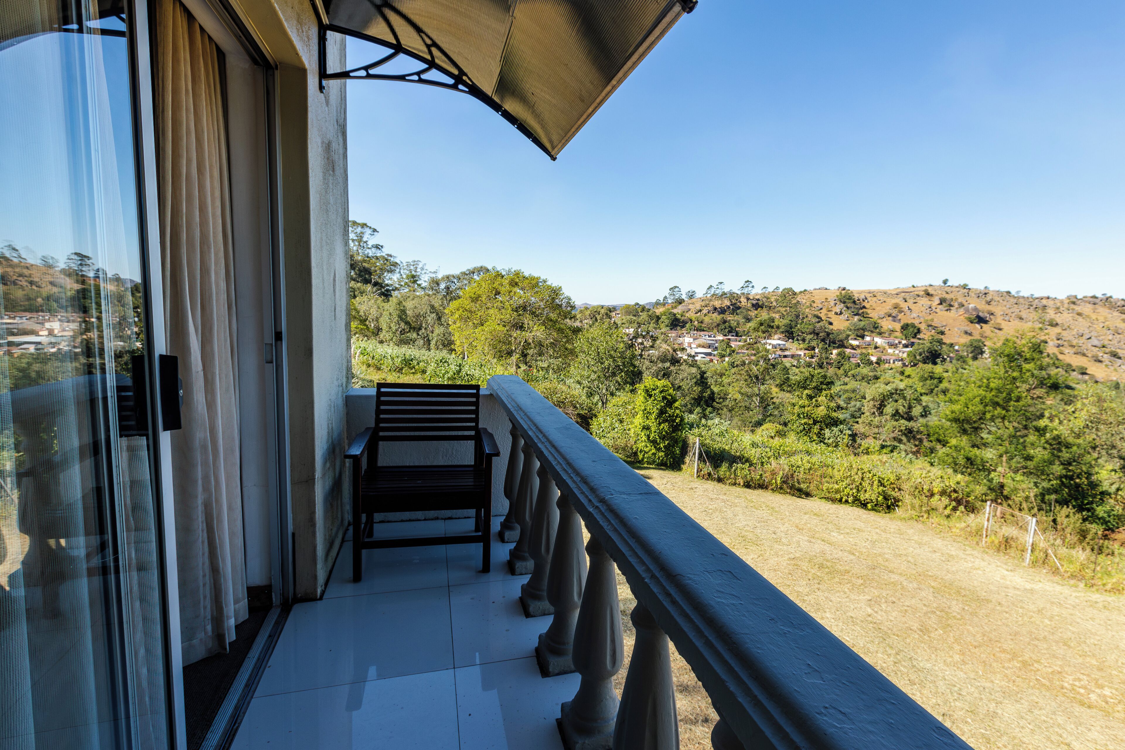 A balcony with a view of a hilly landscape, a bench, and a glass door.
