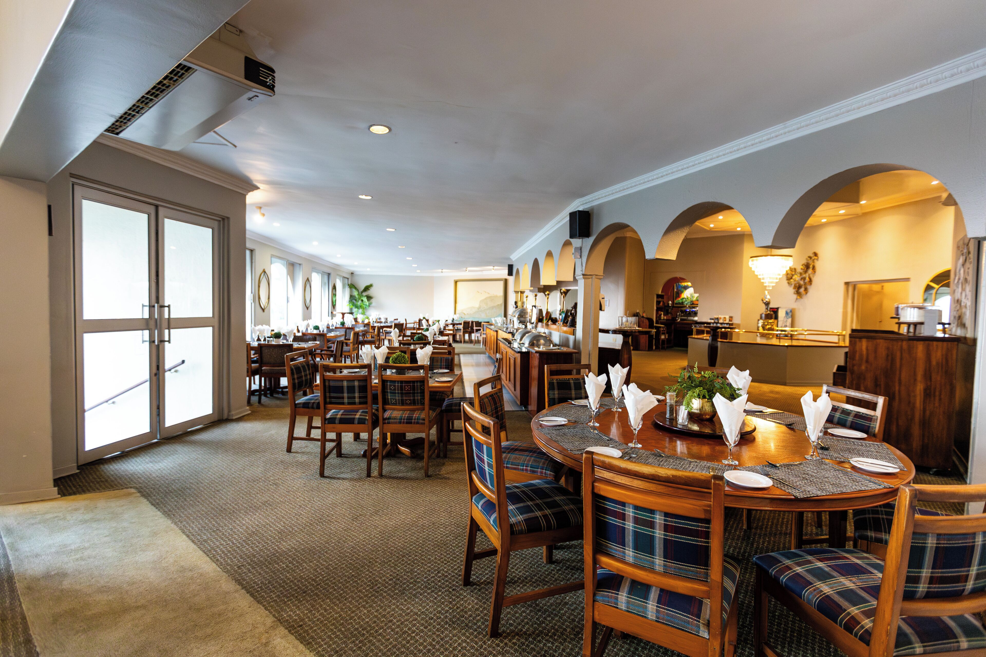 A spacious hotel dining area with multiple tables, chairs, and a bar.