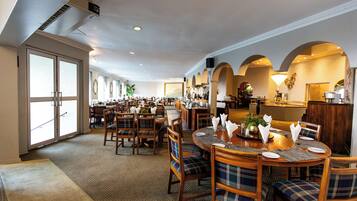 A spacious hotel dining area with multiple tables, chairs, and a bar.