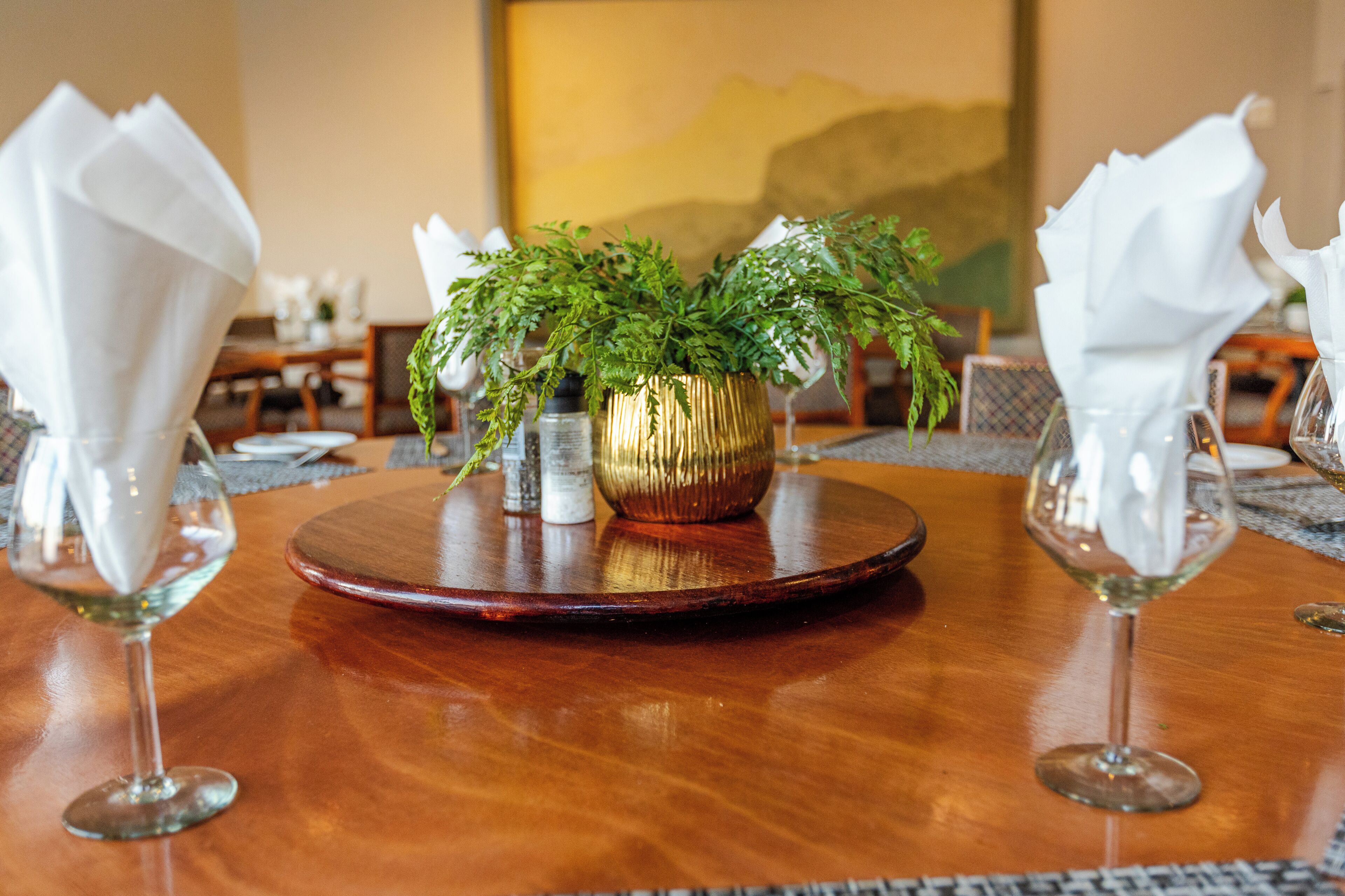 Una mesa de comedor con una planta en el centro, dos copas de vino y un mantel individual.