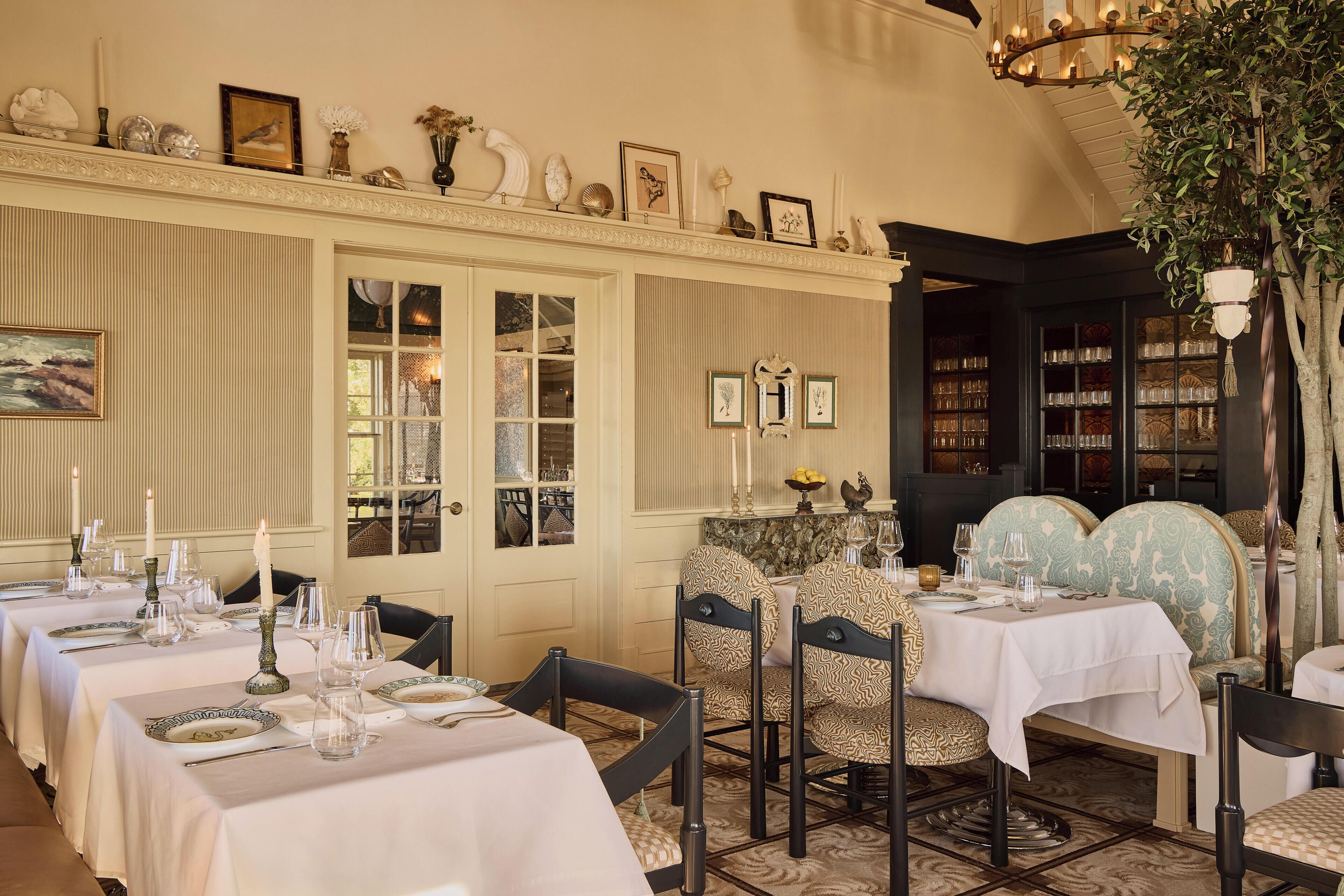 A dining area with tables set for service, chairs with patterned upholstery, and a chandelier.