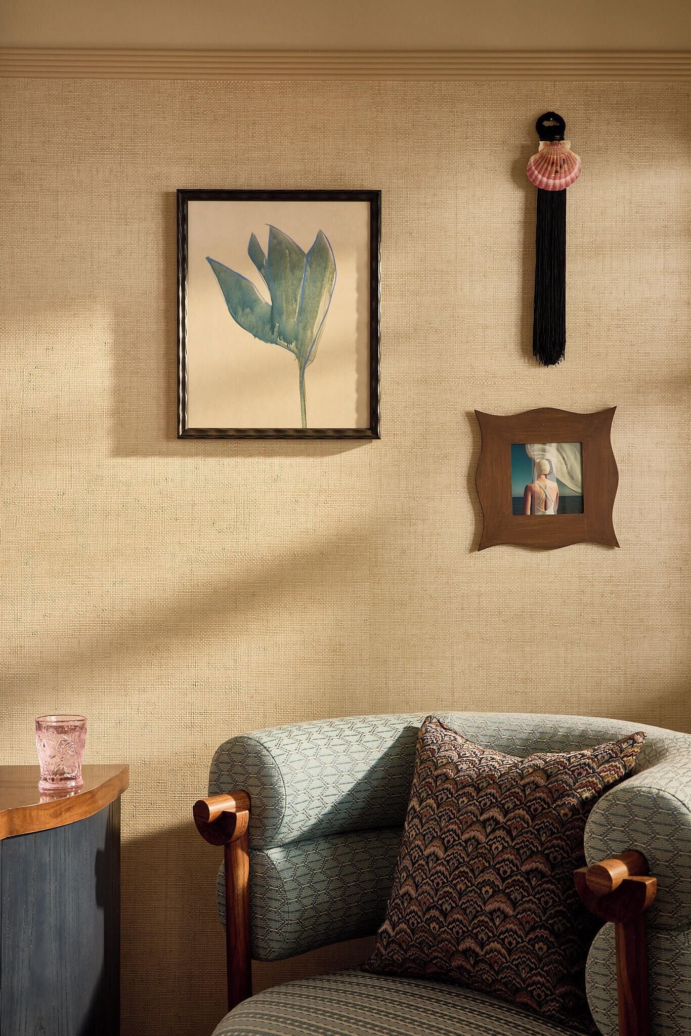 A room with a framed artwork, a hanging ornament, and a patterned cushion on a chair.