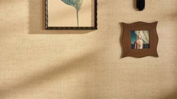 A room with a framed artwork, a hanging ornament, and a patterned cushion on a chair.