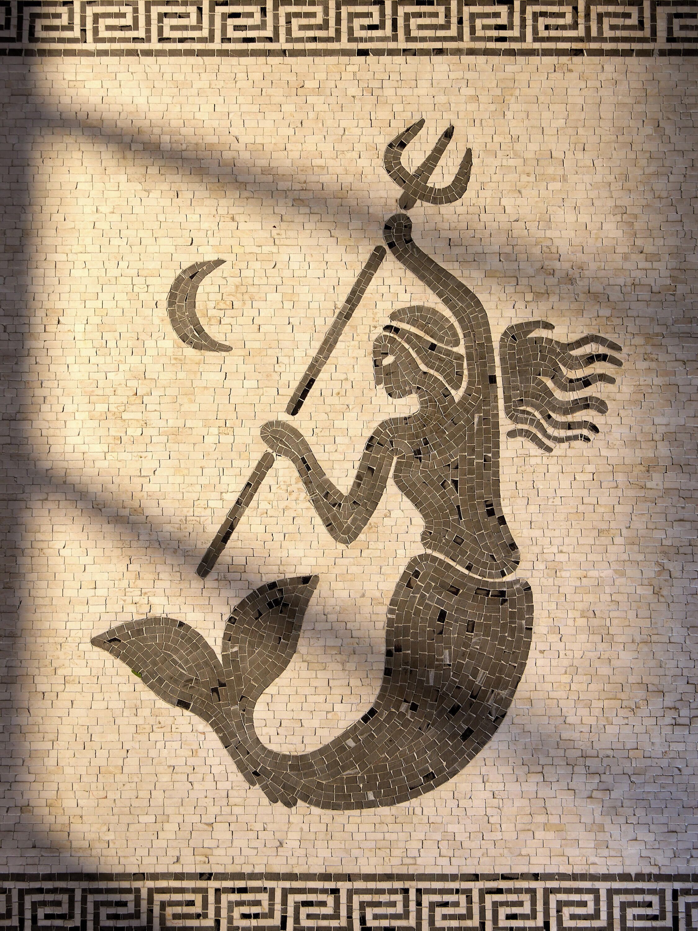 Une mosaïque représentant une figure dotée d’un trident, d’une queue et d’ailes, le tout sur fond de mur de briques.