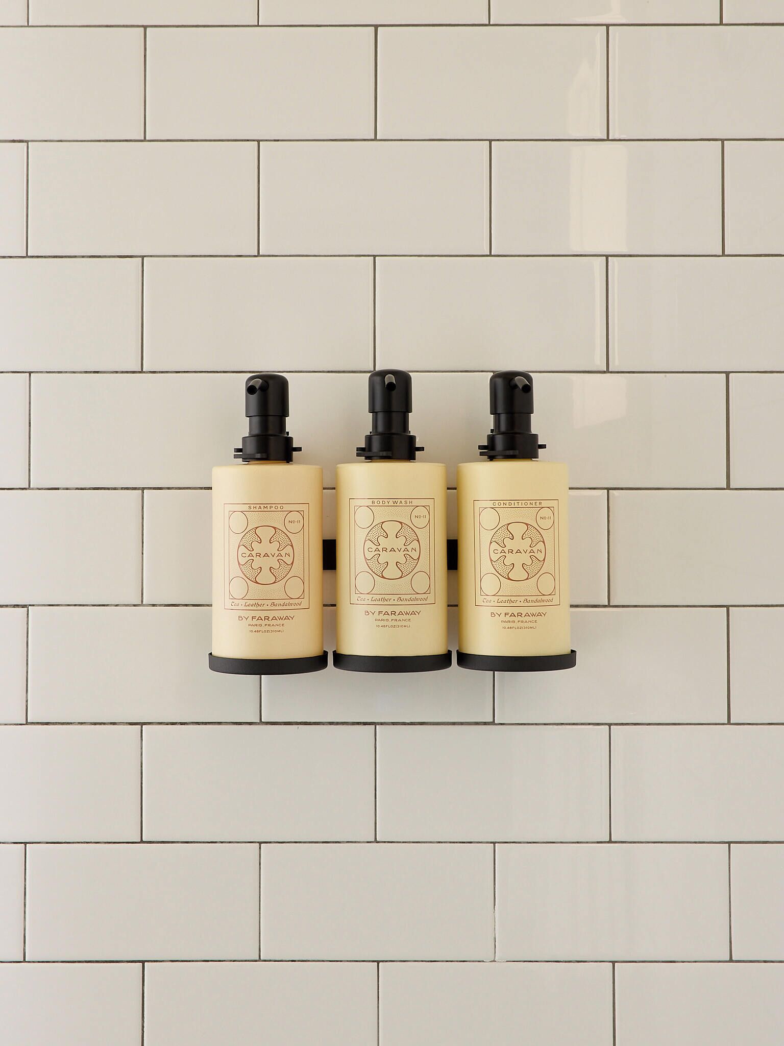 Tre flasker Caravan fra Faraway bodyscrub og balsam på en hvid flisevæg.