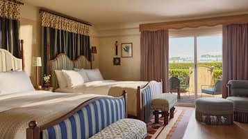 A hotel room with two beds, a balcony with chairs, and a view of greenery.