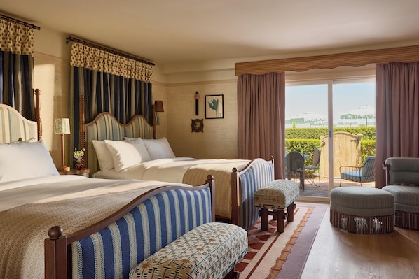 Habitación de hotel con dos camas, un balcón con sillas y vistas a zonas verdes.