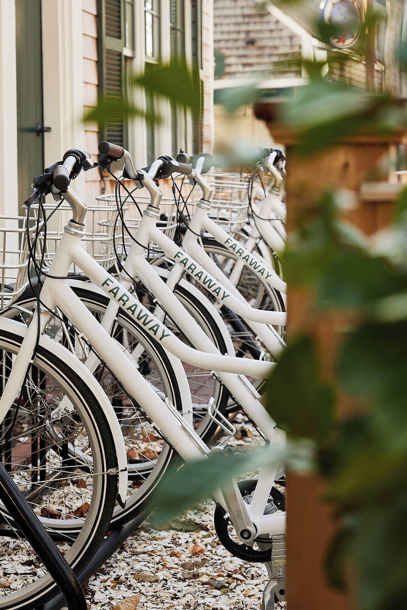 A row of bicycles with 'FARAWAY' branded on the frame, parked in front of a building with a brick facade and green shutters.