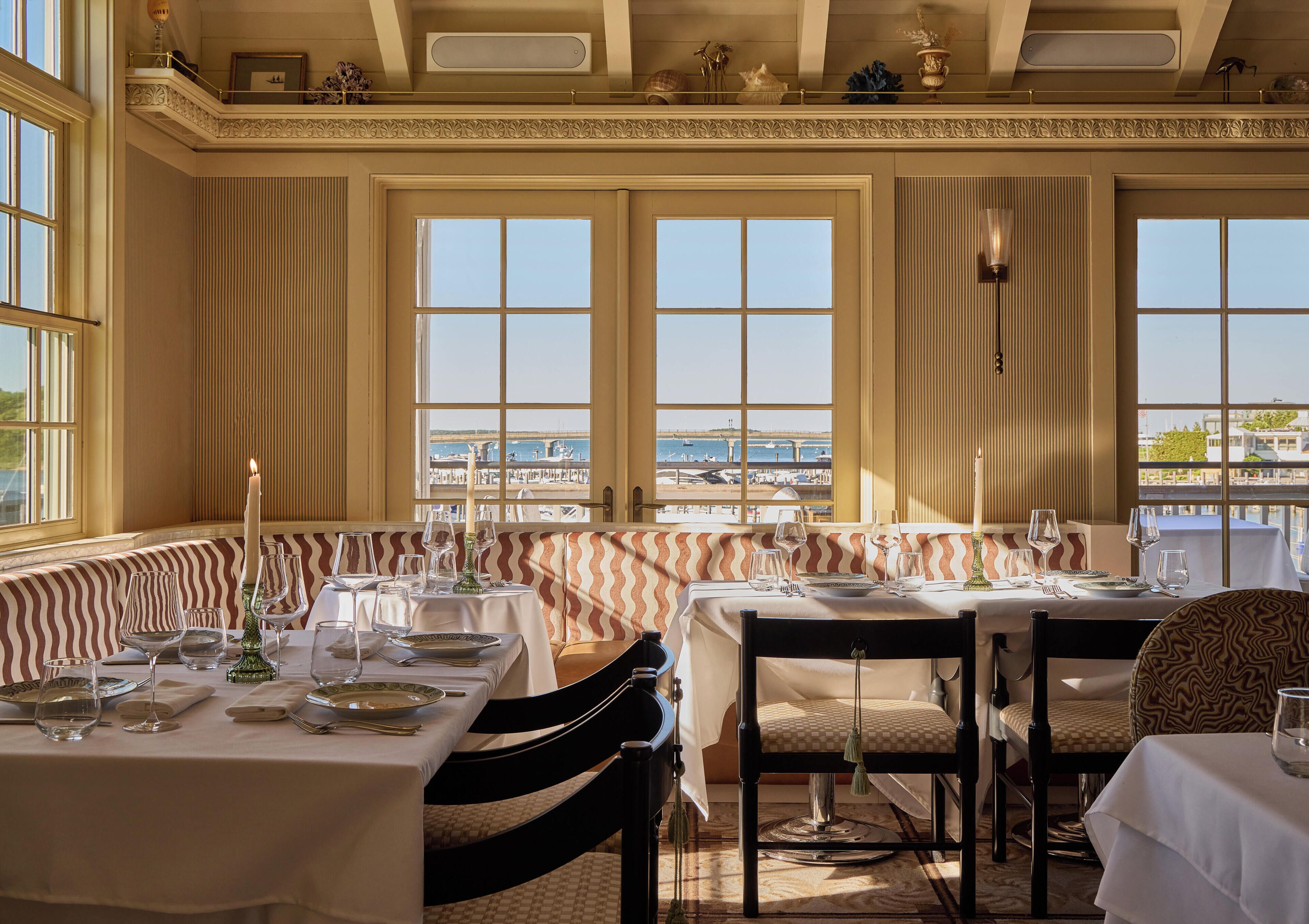 A dining area with a view of the marina, large windows, and a high ceiling with decorative moldings.