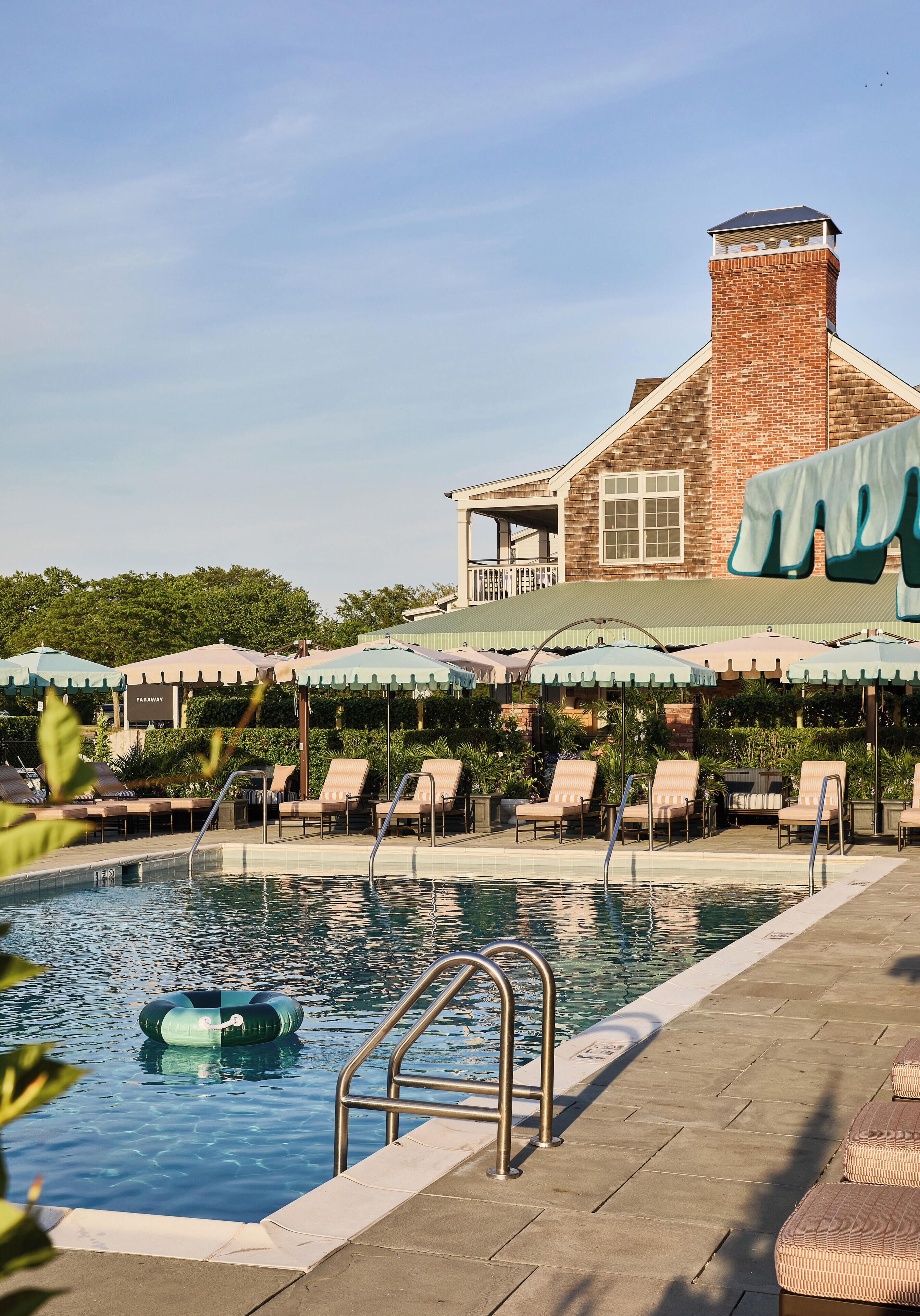 A pool area with lounge chairs, a pool ladder, and umbrellas.